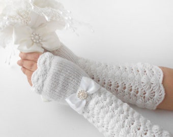 May include: White crocheted fingerless gloves with a white satin bow and a pearl-like button. The gloves have a scalloped edge.