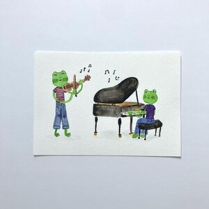 May include: Watercolor illustration of two green frog musicians. One frog plays a violin, the other plays a black grand piano. Musical notes float above the instruments. The frogs wear colorful clothing.