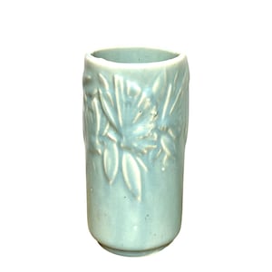 Puede incluir: Un jarrón de cerámica azul claro con forma cilíndrica. El jarrón presenta un diseño floral en relieve en su superficie. El jarrón mide aproximadamente 13 cm de alto y tiene un acabado liso y brillante. Adecuado para flores o como objeto decorativo.