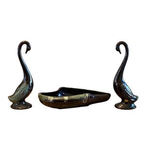 Puede incluir: Un juego de tres figuras de cisnes de cerámica y un plato a juego. Los cisnes son de color marrón oscuro con detalles turquesa, y el plato es de un color similar. Las figuras de cisnes miden unos 20 cm de altura.
