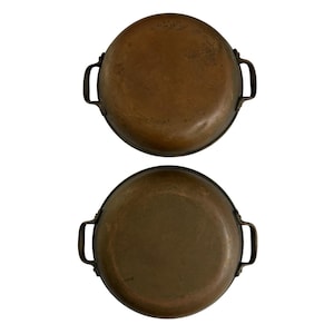 Puede incluir: Dos sartenes antiguas de cobre con asas oscuras. Las sartenes son redondas con una forma ligeramente cóncava y una rica pátina envejecida. Las asas están unidas a los lados de las sartenes. Ideales para cocinar.