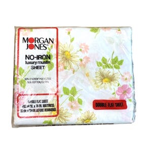 Puede incluir: Una sábana plana doble empaquetada de Morgan Jones. La sábana es blanca con un estampado floral en rosa, amarillo y verde. El embalaje incluye el texto "NO-IRON luxury muslin SHEET" y dimensiones para un colchón de 137 cm x 193 cm.