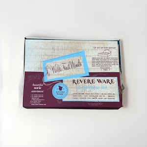 Puede incluir: Una caja de juego de utensilios de cocina Revere Ware vintage. La caja presenta una combinación de colores azul y burdeos con las palabras "World's Finest Utensils" y "Revere Ware" en una fuente estilizada. La caja también incluye texto sobre las características de los utensilios de cocina.