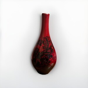 May include: A tall, teardrop-shaped red vase with a narrow neck. The vase features a dark, tree-like pattern across its surface. The base of the vase is a darker shade of brown. The vase is likely made of glass or ceramic.