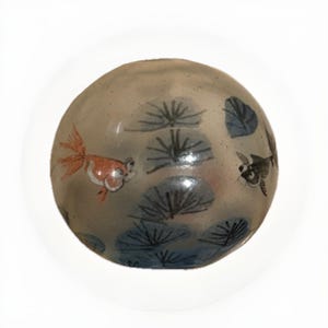 Könnte beinhalten: Runder, dekorativer Glasgegenstand mit handgemaltem Design. Das Design zeigt einen Goldfisch und einen dunklen Fisch, die zwischen blauen und grauen Seerosen schwimmen. Das Objekt ist hellgrau und hat eine glänzende Oberfläche.