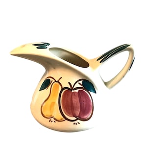 May include: Cream-colored ceramic pitcher with a handle and spout. The pitcher is decorated with a yellow pear and a red and purple apple. Green leaves accent the fruit. The handle has green stripes.