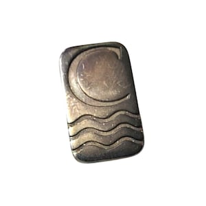 May include: A rectangular, silver-toned metal pin with a curved design at the top and wavy lines at the bottom. The top design resembles a crescent moon and the letter "C". The pin is likely a decorative accessory.
