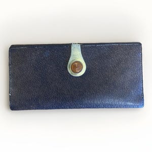 May include: A navy blue wallet with a textured surface. The wallet has a clasp with a circular emblem. The clasp is a light green color with a copper-colored emblem in the center.