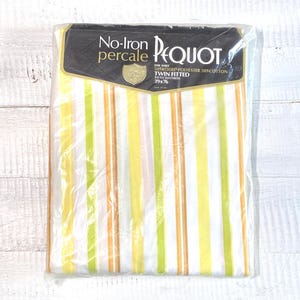 May include: A packaged twin fitted sheet with vertical stripes in yellow, green, and orange. The sheet is labeled "No-Iron Percale PEQUOT" and is designed to fit a 39 x 76 inch mattress. The sheet is made of 50% polyester and 50% cotton.