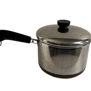 May include: A stainless steel saucepan with a lid and a black handle. The pot has a dark brown base and a black knob on the lid. The handle has a loop at the end. Kitchen cookware.