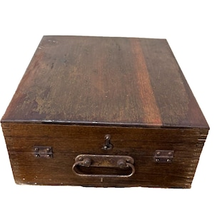 May include: A rectangular wooden box with a dark brown finish. The box has a metal handle and hinges, and a small latch. The wood shows signs of wear, giving it a vintage appearance. The box is closed.