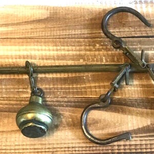 May include: Vintage brass balance scale featuring a curved hook, a hanging weight, and a pivoting arm. The scale has a classic design, showing signs of age and use. The scale is set against a wooden background.