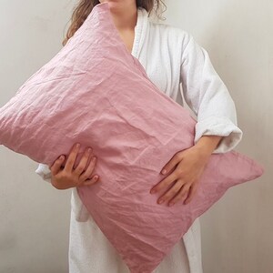 Puede incluir: Una funda de almohada de lino rosa suave sostenida por una persona que lleva una bata blanca. La funda de almohada est&aacute; hecha de una tela natural y transpirable.