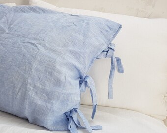 May include: A light blue linen pillow with white ties on a white bed. The pillow has a textured surface and is made of natural fibers.