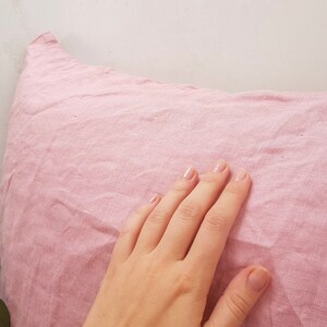 Puede incluir: Una funda de almohada de lino rosa suave con una superficie lisa y texturizada.