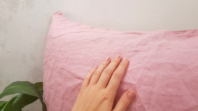 Puede incluir: Una funda de almohada de lino rosa suave con una superficie lisa y texturizada.