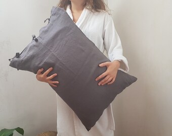 May include: A gray linen pillowcase with ties. The pillowcase is being held by a person wearing a white robe.