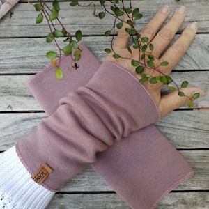 Könnte beinhalten: Ein Paar mauvefarbene Armwärmer aus weichem, dehnbarem Stoff. Die Armwärmer sind hochgekrempelt und haben ein braunes Etikett mit der Aufschrift "HAND".