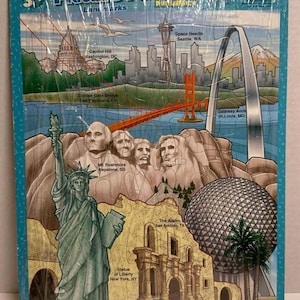Może przedstawiać: Prostokątne puzzle przedstawiające kolaż zabytków Stanów Zjednoczonych, w tym Statuę Wolności, górę Rushmore, Gateway Arch, most Golden Gate, Space Needle, Kapitol, Alamo oraz centrum Epcot.