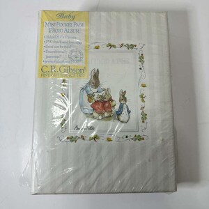 Op de afbeelding: Een nieuw babyfotoalbum met een Peter Rabbit-illustratie. Het album is wit met verticale strepen en een decoratieve rand. De omslag bevat de tekst "Baby Mini Pocket Page Photo Album" en het C.R. Gibson-logo.