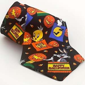 May include: A black necktie featuring a repeating pattern of Looney Tunes characters including Tweety Bird and Bugs Bunny, orange jack-o'-lanterns, candy corn, and bats. The text "HAPPY HALLOWEEN" and "TWICK TWEEET" is printed on the fabric.