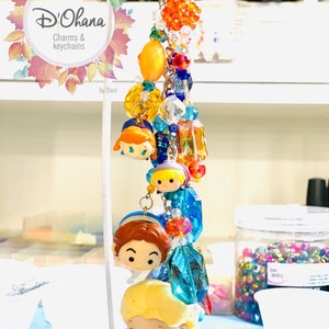 May include: A colorful charm keychain featuring Disney characters with a variety of beads, including clear, orange, yellow, blue, and red. The keychain is labeled "D'Ohana Charms & Keychains by Dani".