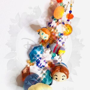 May include: A colorful beaded keychain with a variety of charms, including small figurines of characters from the animated film Frozen. The keychain features a blue, orange, and yellow color scheme and includes a silver key ring. The text "by Dani" is visible at the bottom of the image.