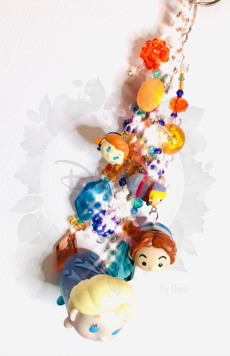 May include: A colorful beaded keychain with a variety of charms, including small figurines of characters from the animated film Frozen. The keychain features a blue, orange, and yellow color scheme and includes a silver key ring. The text "by Dani" is visible at the bottom of the image.