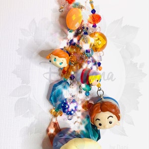 May include: A colorful keychain featuring a variety of beads and charms, including a group of cartoon characters with large eyes. The characters are from the Disney movie Frozen. The keychain also includes a silver key ring and the text "by Dani".