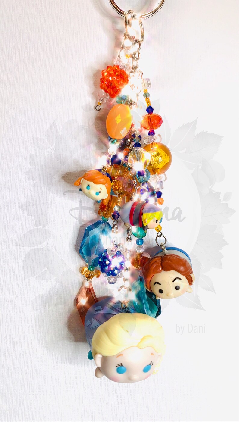 May include: A colorful keychain featuring a variety of beads and charms, including a group of cartoon characters with large eyes. The characters are from the Disney movie Frozen. The keychain also includes a silver key ring and the text "by Dani".