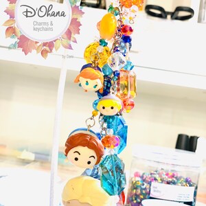 May include: A colorful charm bracelet featuring a variety of beads, including clear crystals, orange, yellow, and blue beads. The bracelet also features four small, cartoon-style character charms. The bracelet is labeled "D'Ohana Charms & Keychains by Dani."