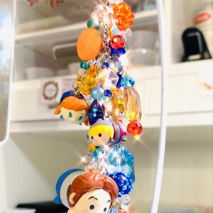 May include: A colorful keychain featuring a variety of charms, including small figurines of characters from the Disney movie Frozen. The keychain is made with beads, crystals, and metal accents. The keychain is labeled "D'Ohana Charms & Keychains by Dani."
