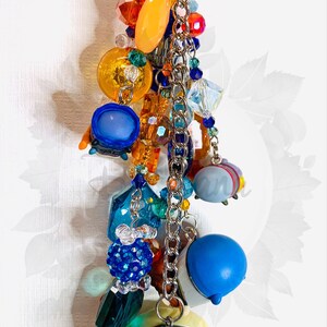 May include: A colorful charm keychain with a blue, yellow, and white character charm. The keychain features a variety of beads, including clear crystals, orange, blue, and green beads, and a silver chain.
