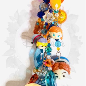 May include: A colorful charm bracelet with a variety of beads, including clear crystals, orange and yellow beads, and blue beads. The bracelet also features several small, colorful figurines of characters from the animated film Frozen.
