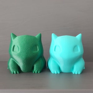 Könnte beinhalten: Zwei kleine, 3D-gedruckte Figuren eines Pokemon-Charakters. Die Figur links ist grün und die Figur rechts ist blau.