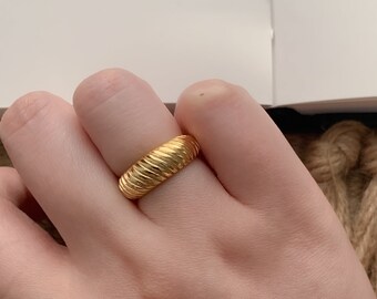 May include: A gold-toned ring with a textured, ridged design. The ring is worn on a finger.