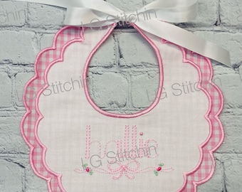 Könnte beinhalten: Rosa-weißes Gingham-Baby-Lätzchen mit gewellten Rändern und gesticktem "Hallo" mit Schleife und Blumen.