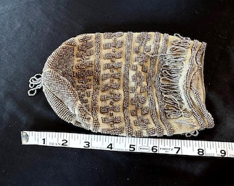 May include: A vintage beaded purse with a geometric pattern and fringe detail. The purse is made of silver-colored beads and measures approximately 7 inches in length.