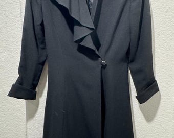 May include: Black long coat with a unique ruffled collar and a single button closure. The coat has long sleeves with folded cuffs. The brand name "Tahar" is visible on the label. A classic and elegant outerwear piece.