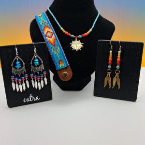 May include: A jewelry set featuring a beaded bracelet with a geometric pattern, a necklace with a gold sun pendant, and two pairs of earrings. One pair has teardrop shapes with turquoise beads and feathers, while the other has dangling feathers.