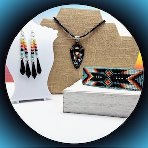 May include: A jewelry set featuring a necklace with a black arrowhead pendant depicting an eagle, a pair of multi-colored beaded dangle earrings with black pointed charms, and a wide woven bracelet with a geometric pattern in black, orange, and blue.