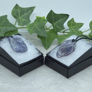 Peut inclure: Deux pendentifs en cristal d'améthyste sur des boîtes en velours noir avec un cordon noir. Les cristaux d'améthyste sont d'une couleur violette profonde et ont une forme naturelle irrégulière.