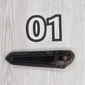 May include: A black, elongated crystal with a polished surface. The number "01" is printed in black above the crystal on a light wood-grain background. The crystal is approximately 5 inches long.