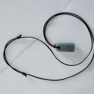 May include: A green stone pendant on a black cord necklace.