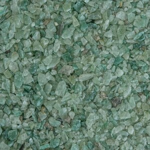 May include: A close-up view of a large quantity of small, translucent green glass pieces. The pieces are irregularly shaped and have a slightly frosted appearance.