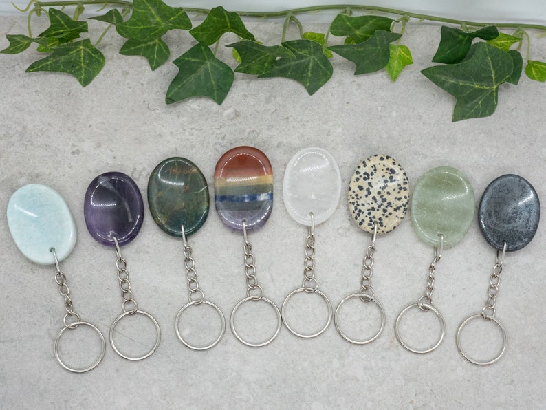 Op de afbeelding: Negen verschillende ovaalvormige edelsteen sleutelhangers met zilveren sleutelringen. De stenen zijn: lichtblauw, paars, groen, rood en blauw gestreept, wit, bruin en wit gevlekt, lichtgroen en grijs.