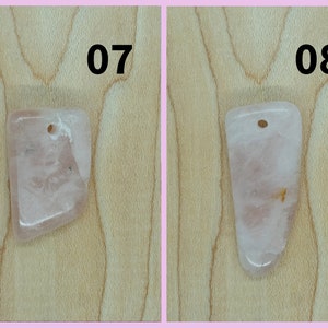 May include: Two pink rose quartz pendants with a hole drilled at the top for stringing. The pendants are on a light brown wooden surface. The numbers 07 and 08 are printed above the pendants.