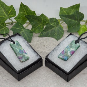 Peut inclure: Deux pendentifs en pierre précieuse verte, rose et blanche avec des cordons noirs dans des boîtes cadeaux noires avec des inserts blancs.