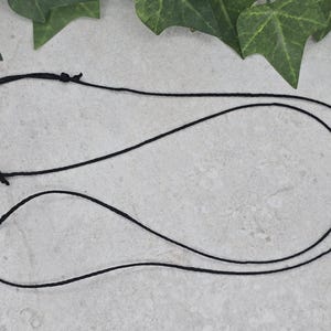 May include: A black cord necklace with a simple design. The cord is doubled and tied together at the top.