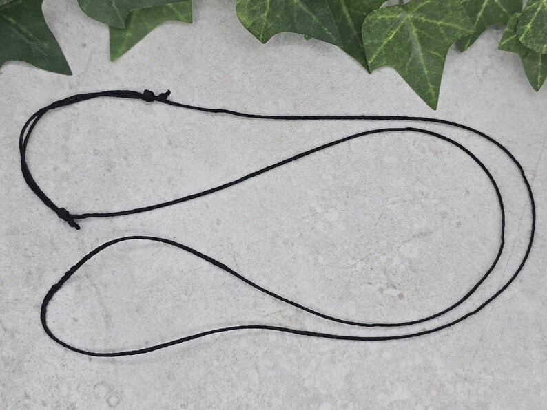 May include: A black cord necklace with a simple design. The cord is doubled and tied together at the top.